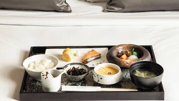 A neatly arranged breakfast tray on a bed with white linens and grey pillows.