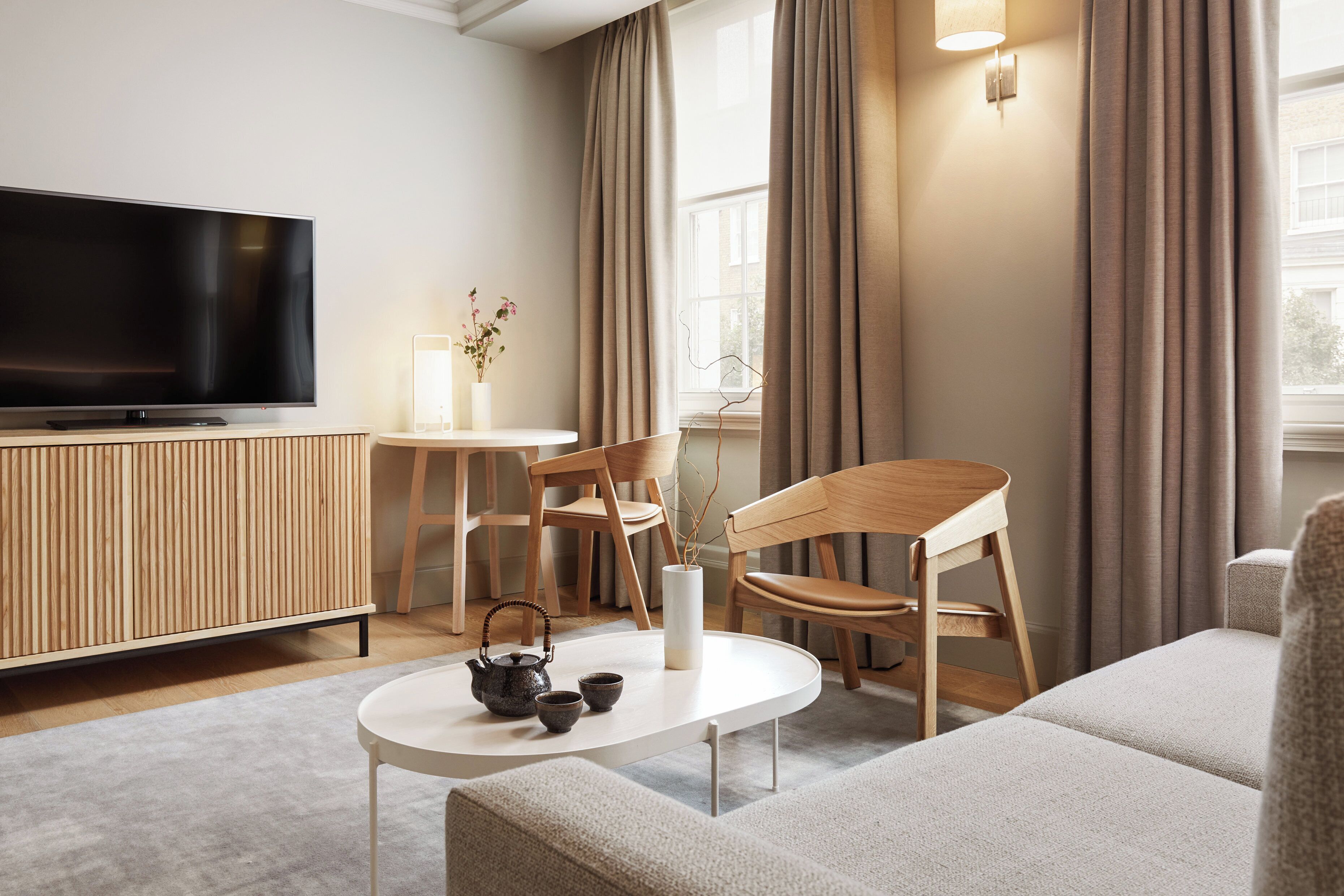 A modern living room with a flat-screen TV, wooden furniture, a round coffee table, and a vase with branches.