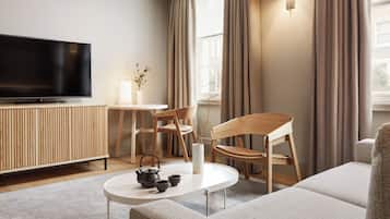 A modern living room with a flat-screen TV, wooden furniture, a round coffee table, and a vase with branches.