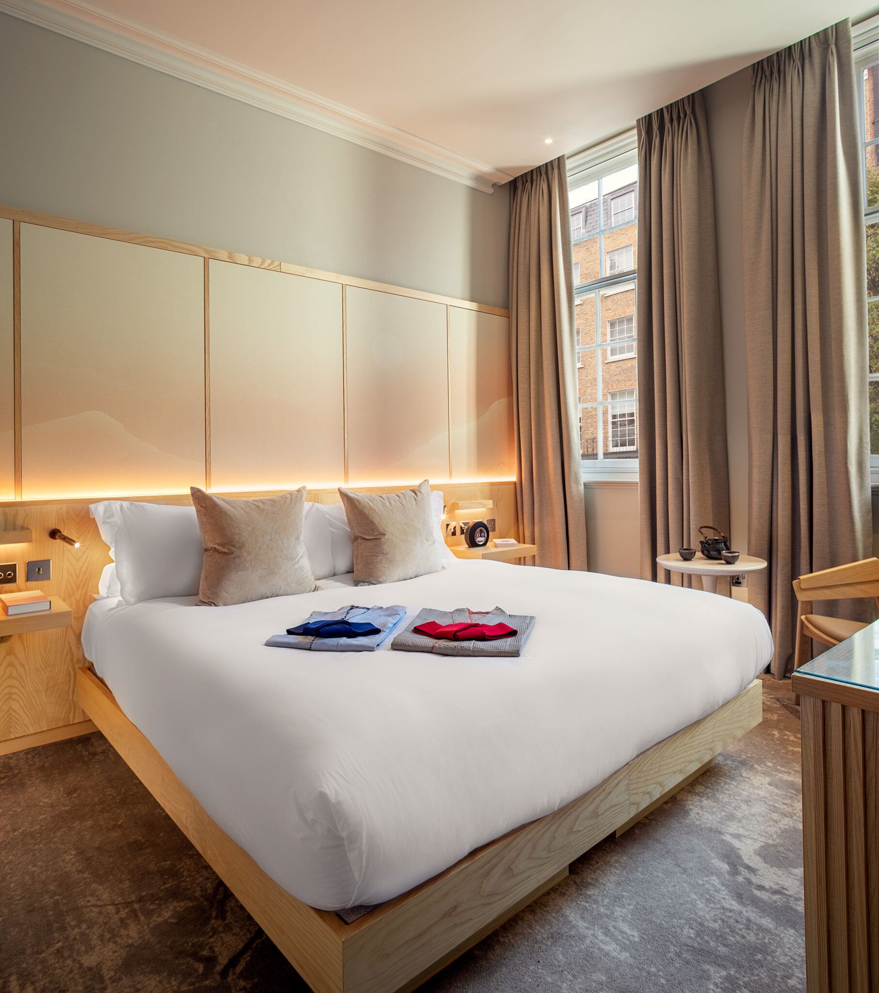 Ein modernes Hotelzimmer mit einem großen Bett, einem Holz-Kopfteil und einem Nachttisch mit Lampe.
