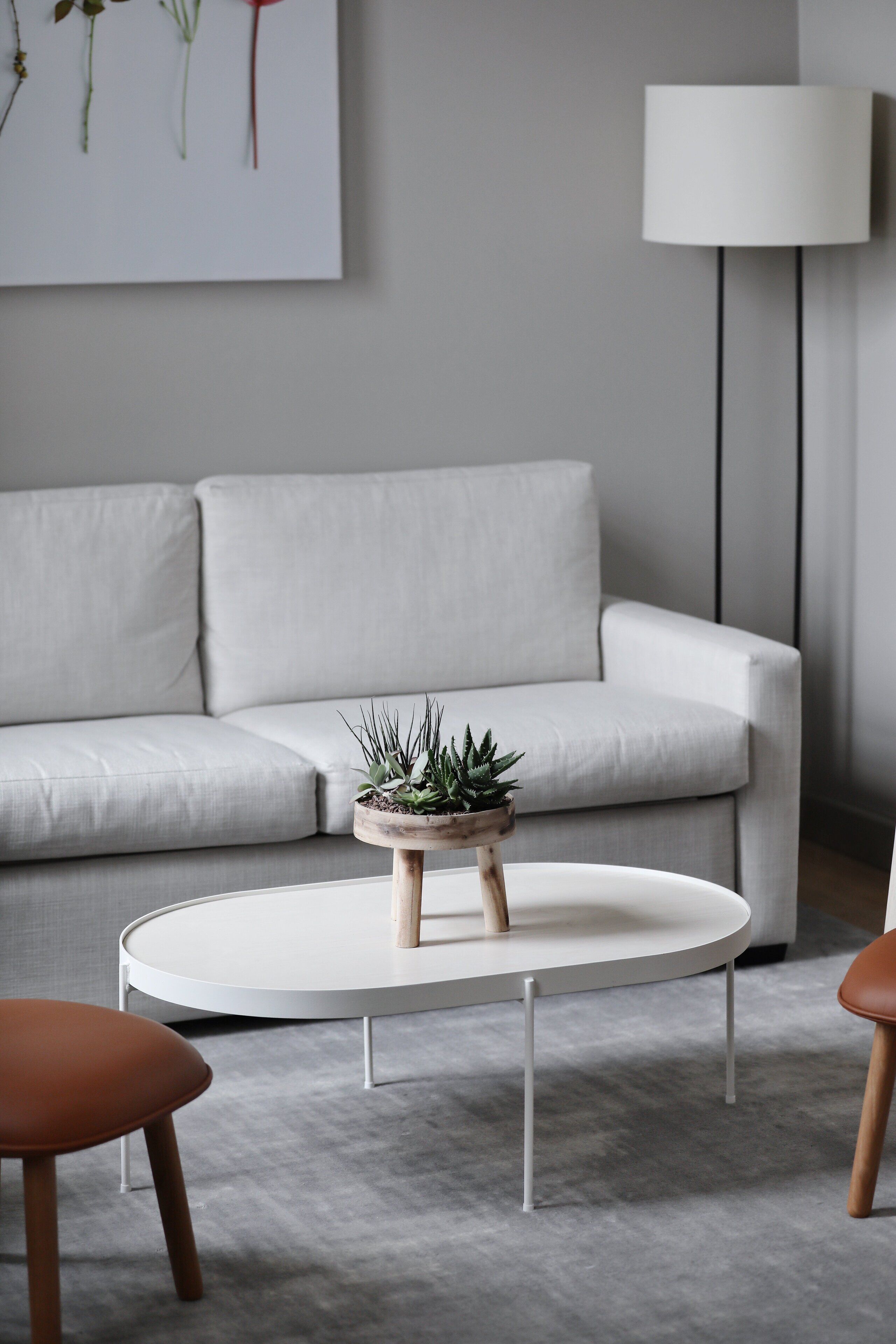 A modern living room with a white sofa, a round white coffee table with a wooden base, and a floor lamp.