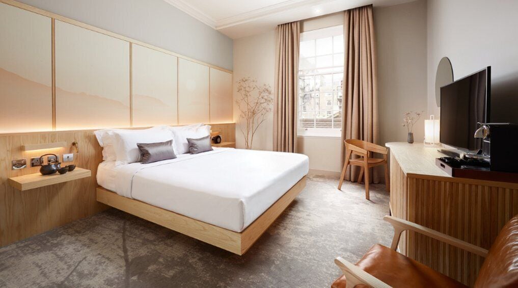 Una habitación de hotel moderna con una cama grande, mesitas de noche, un escritorio, una silla y un televisor.