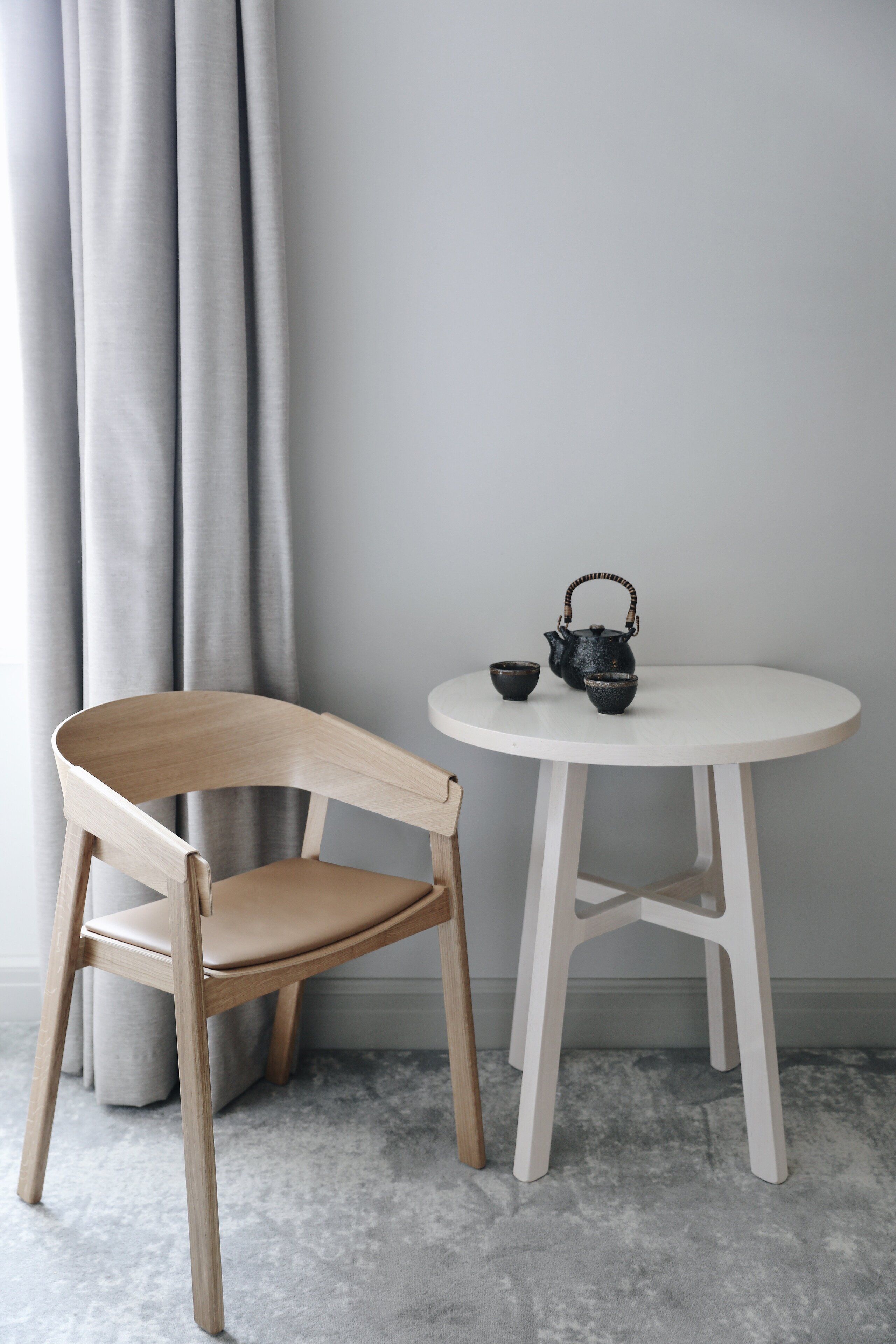 A wooden chair and a white table with a teapot and cups.