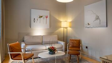 A modern living room with a sofa, two chairs, a coffee table, and a lamp. There are two wall-mounted artworks.