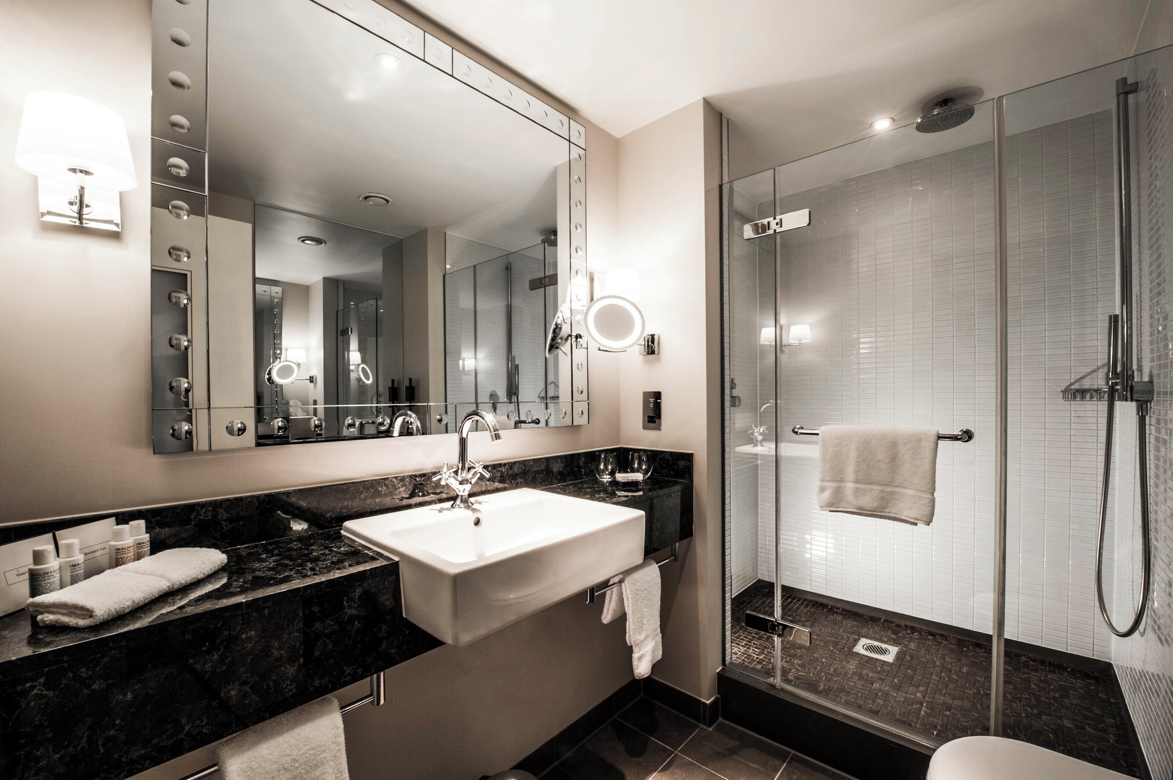 A modern bathroom with a large mirror, vanity, sink, and a glass-enclosed shower.