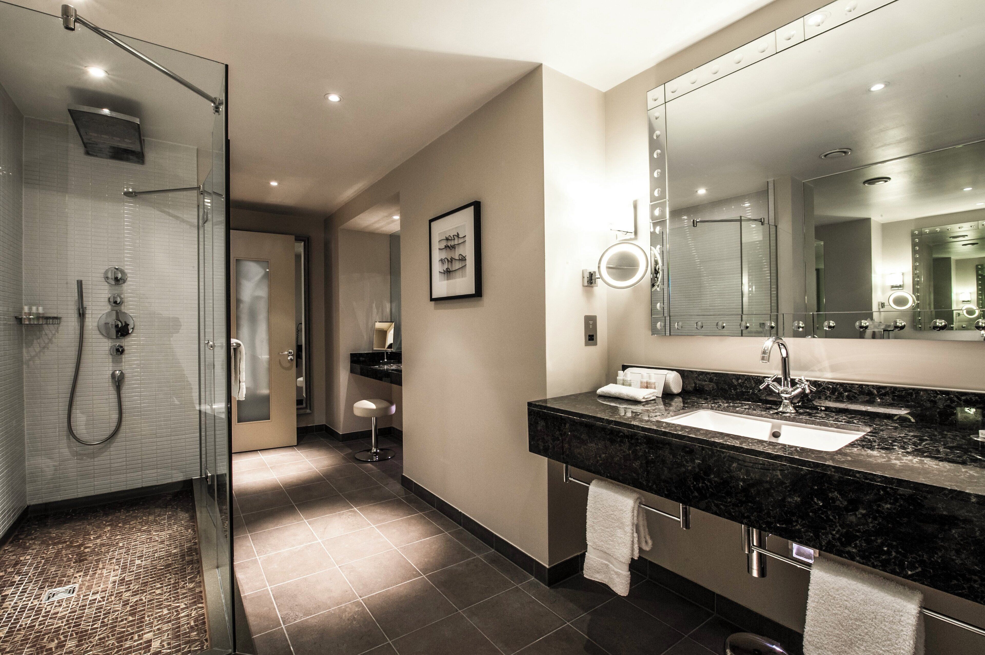 A modern bathroom with a glass-enclosed shower, a large mirror, and a marble countertop.