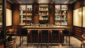A bar area with wooden shelves stocked with bottles, a bar counter, and several bar stools. - The Prince Akatoki London (London)