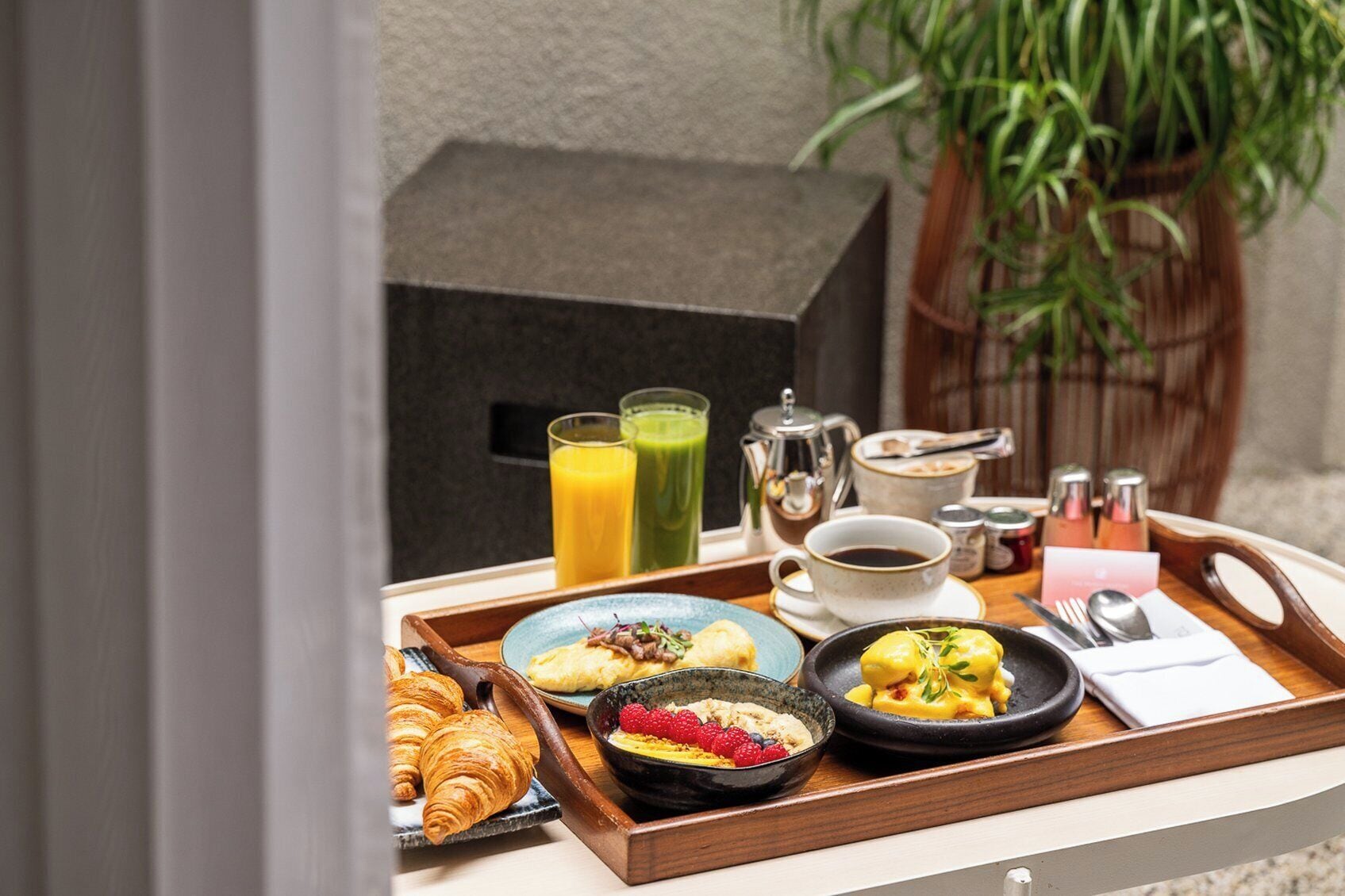 A breakfast tray with croissants, fruit, and a bowl of cereal. There are also two glasses of juice and a coffee pot.