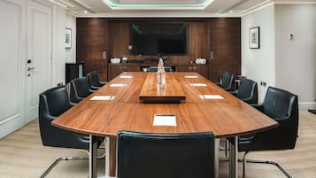 A conference room with a long wooden table, black leather chairs, a flat-screen TV, and a wooden accent wall.