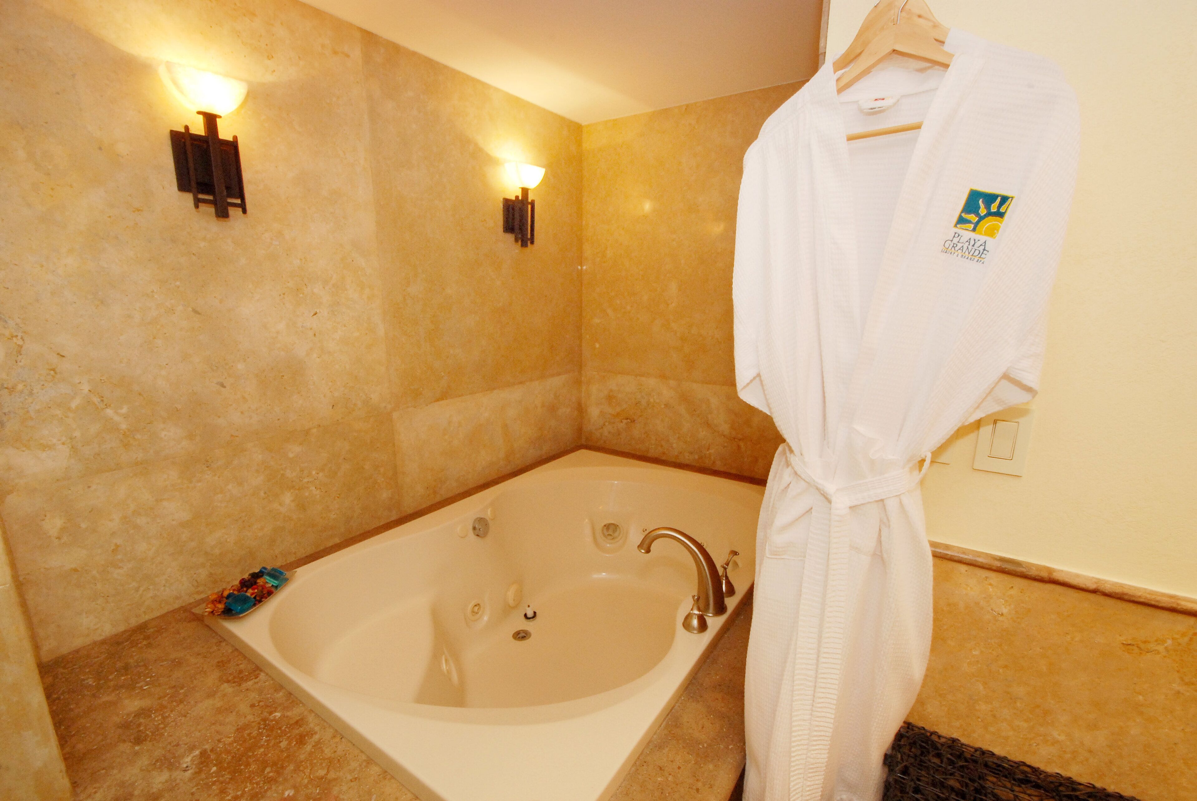 A bathroom with a large bathtub, two wall-mounted lights, and a white robe hanging on a rack.