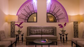 Una sala de estar moderna con un sofá capitonado, dos mesas auxiliares con jarrones y una mesa de centro de vidrio.