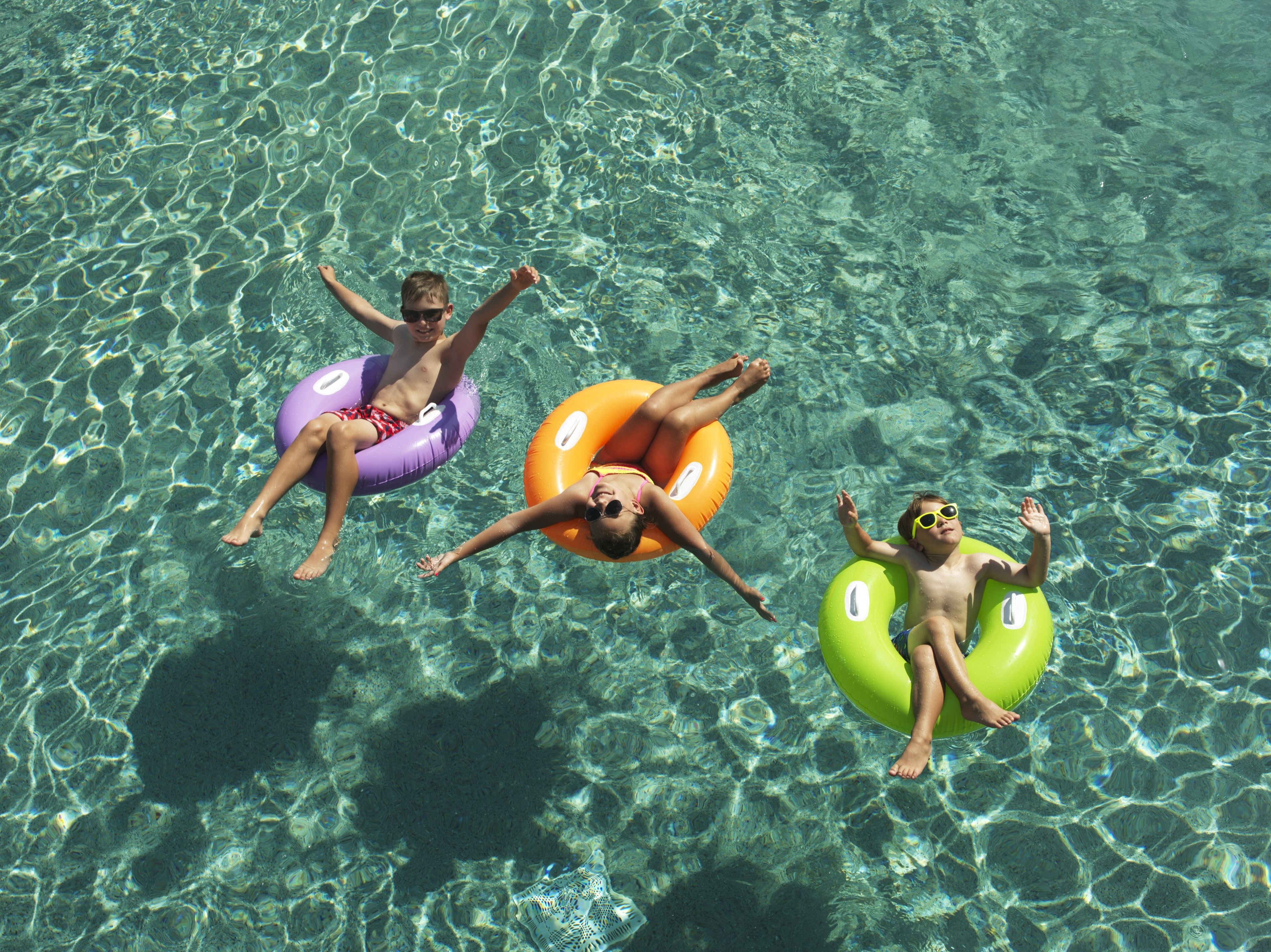 Tres personas flotando en círculos inflables en agua cristalina.