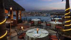 An outdoor dining area with round tables, chairs, and a view of a cityscape and water.