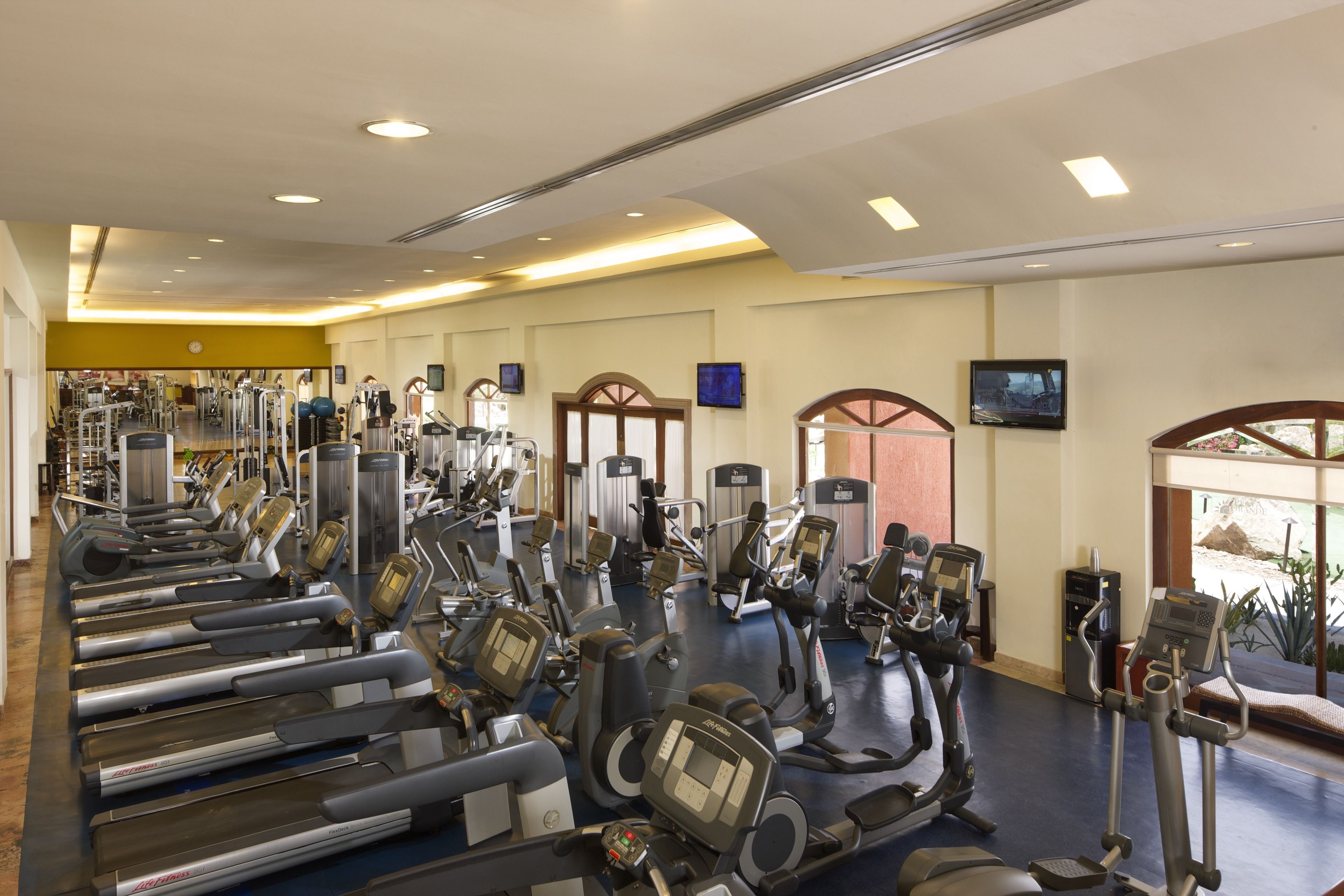 A gym with various exercise machines, including treadmills and elliptical trainers, arranged in rows.
