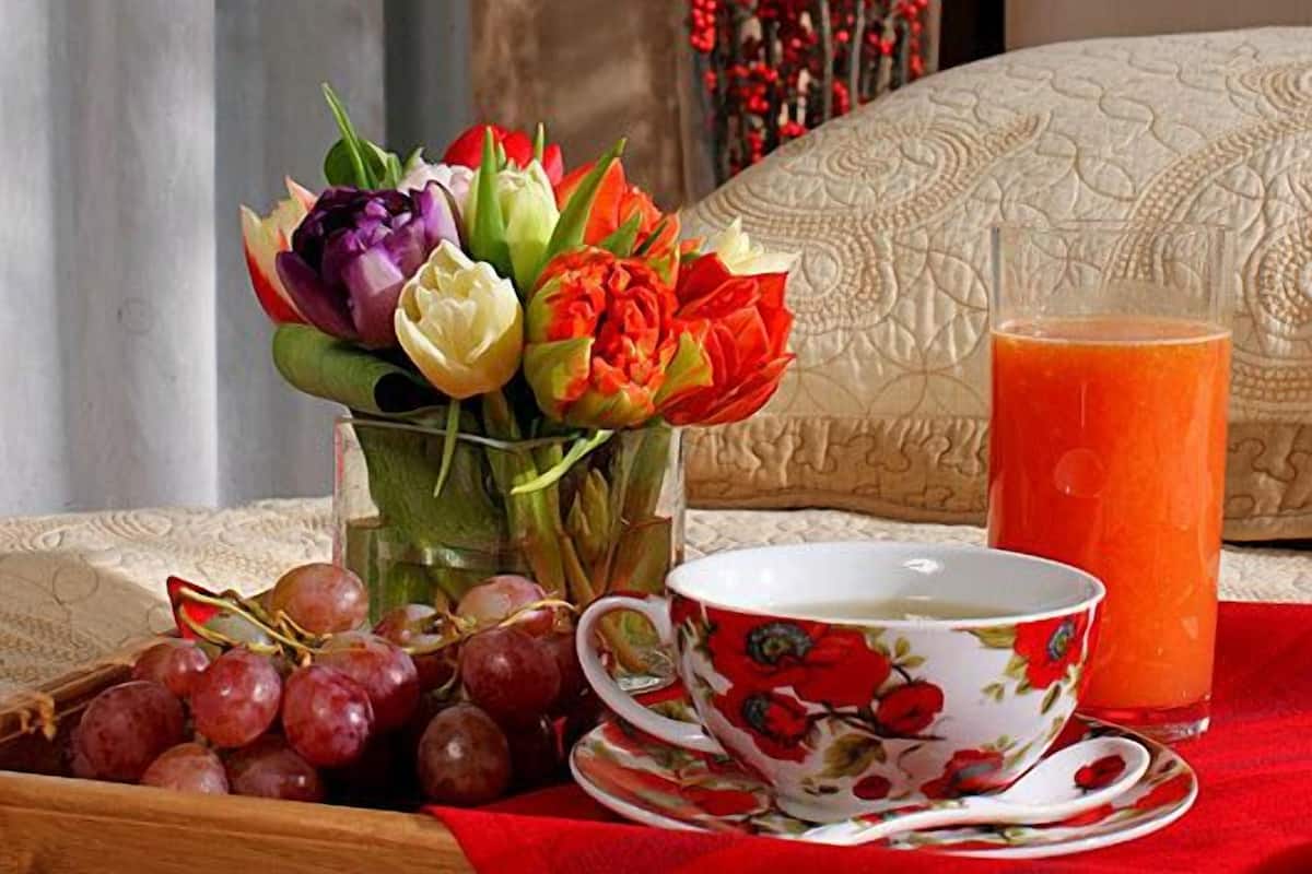 Ein Frühstücksbrett mit einer Blumenkomposition, einer Tasse, einem Glas Orangensaft und Trauben auf einem Tisch mit einer roten Tischdecke.