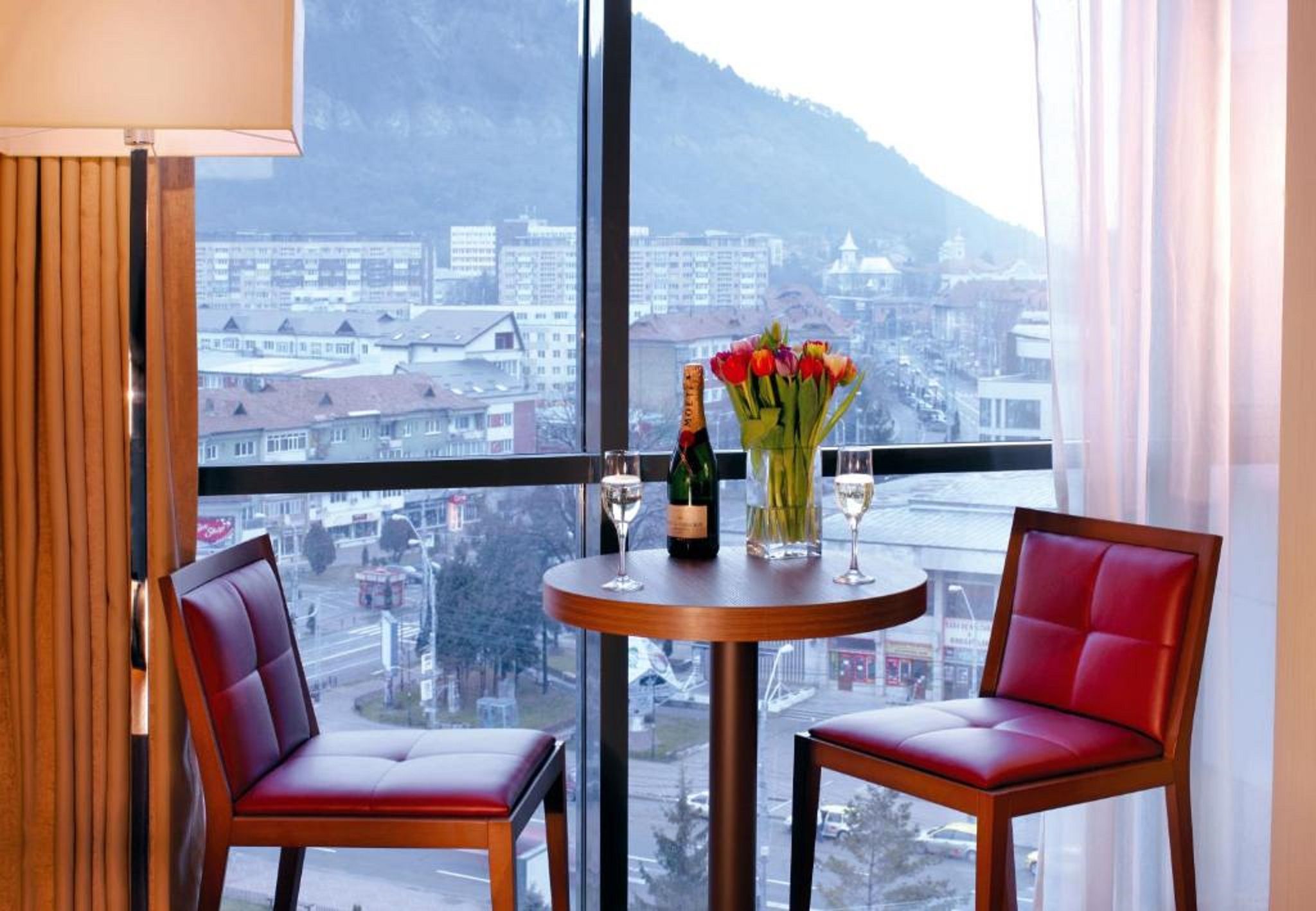 A room with two red leather chairs, a small wooden table with a bottle of champagne, a glass, and a vase of flowers.