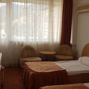 Ein Hotelzimmer mit einem Bett, zwei Sesseln, einem kleinen Tisch und einem Fenster mit transparenten Vorhängen.