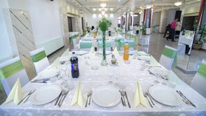 A banquet hall with tables set for a formal event, featuring white tablecloths, green sashes, and clear glassware. - Hotel Seneca (Baia Mare)