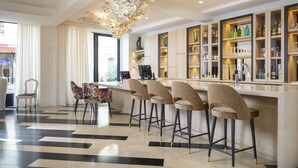 A modern bar area with a bar counter, four bar stools, and a decorative ceiling light fixture. - Hotel Des Champs Elysees (Paris)