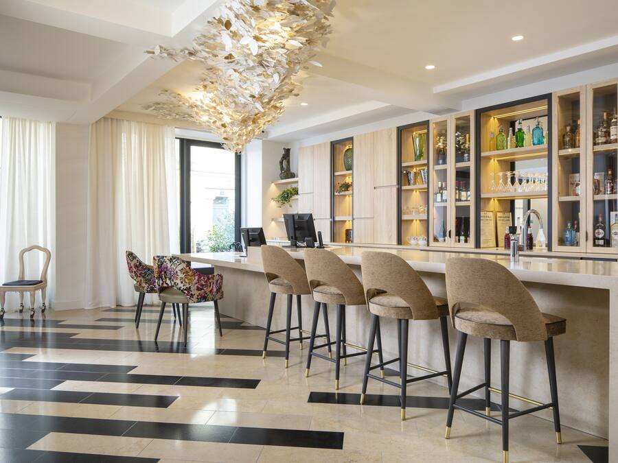 A modern bar area with a bar counter, four bar stools, and a decorative ceiling light fixture.