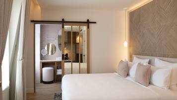 Habitación de hotel con una cama grande, cabecera de madera, espejo, baño pequeño y puerta corredera.