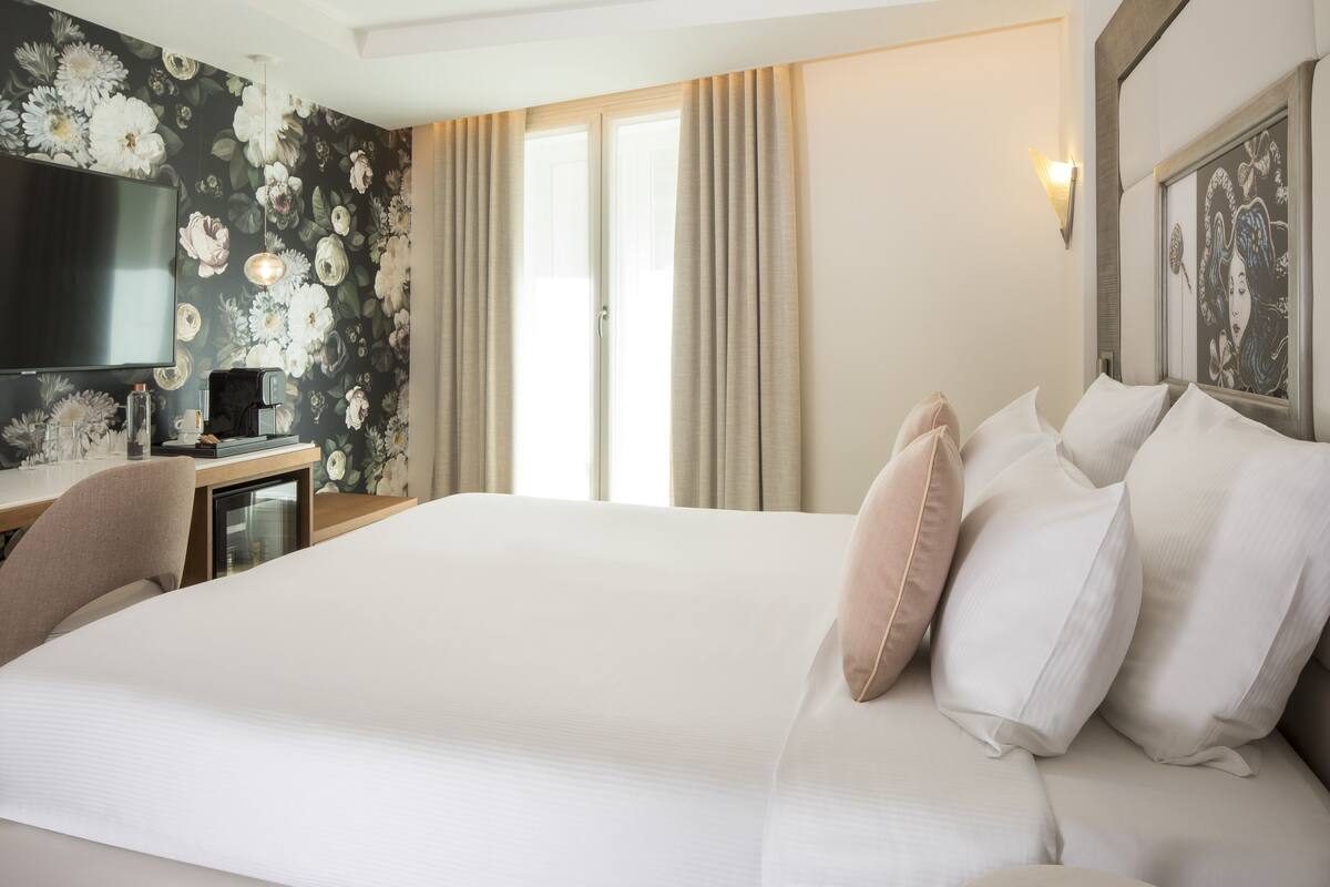 Une chambre d’hôtel avec un grand lit, un bureau avec une machine à café, une télévision et un papier peint à motifs floraux.