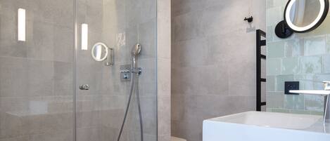 Un baño moderno con ducha de vidrio, lavamanos blanco y espejo con marco redondo.