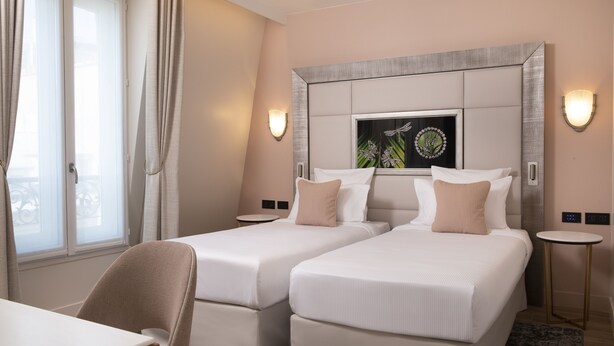 A hotel room with two beds, a small table, and a chair. There is a window with curtains, a wall-mounted artwork, and two wall sconces. - Hotel Des Champs Elysees (Paris)