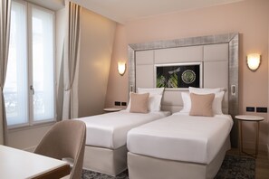 A hotel room with two beds, a small table, and a chair. There is a window with curtains, a wall-mounted artwork, and two wall sconces. - Hotel Des Champs Elysees (Paris)