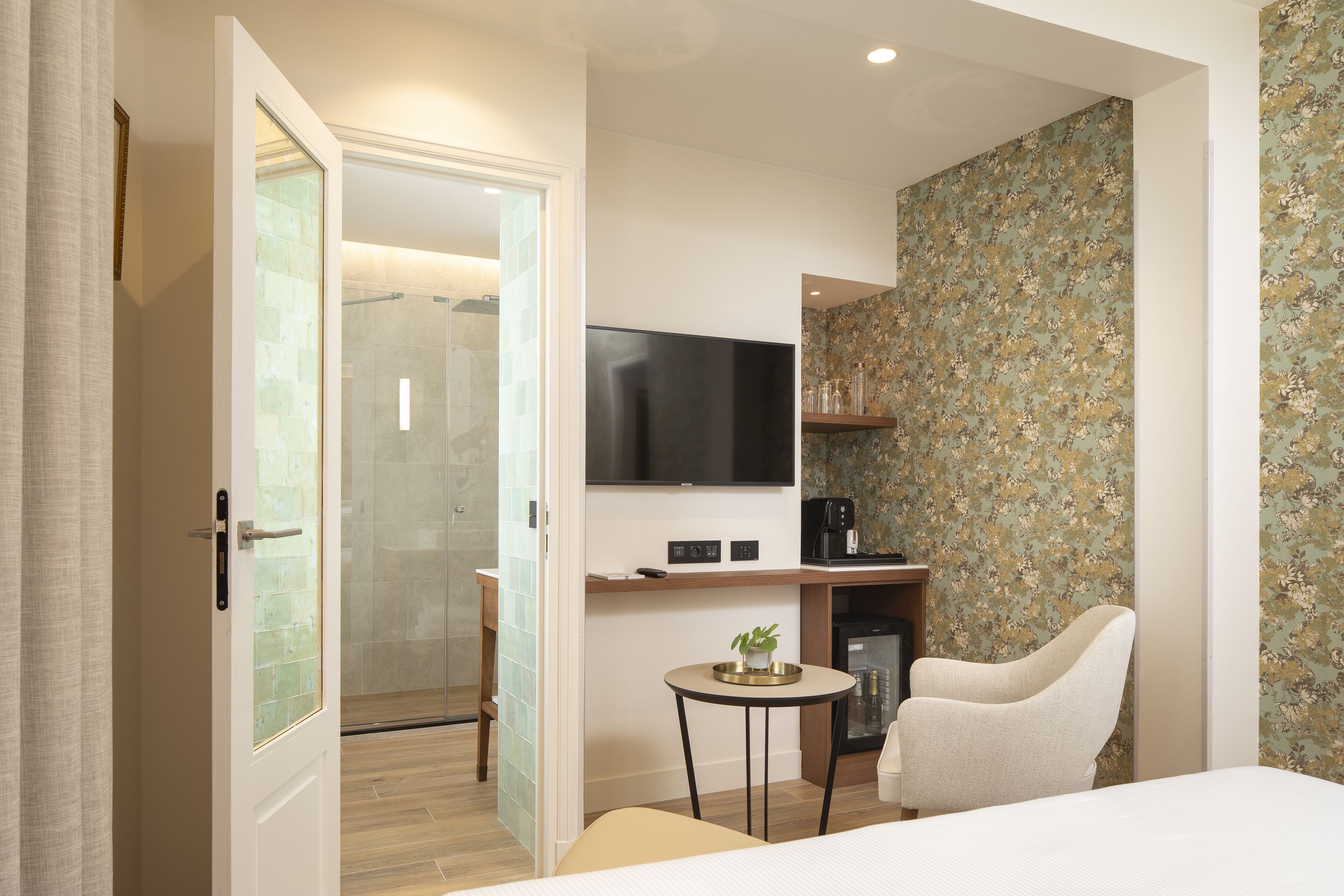 Habitación de hotel moderna con ducha, televisión, cafetera y papel tapiz con estampado floral.