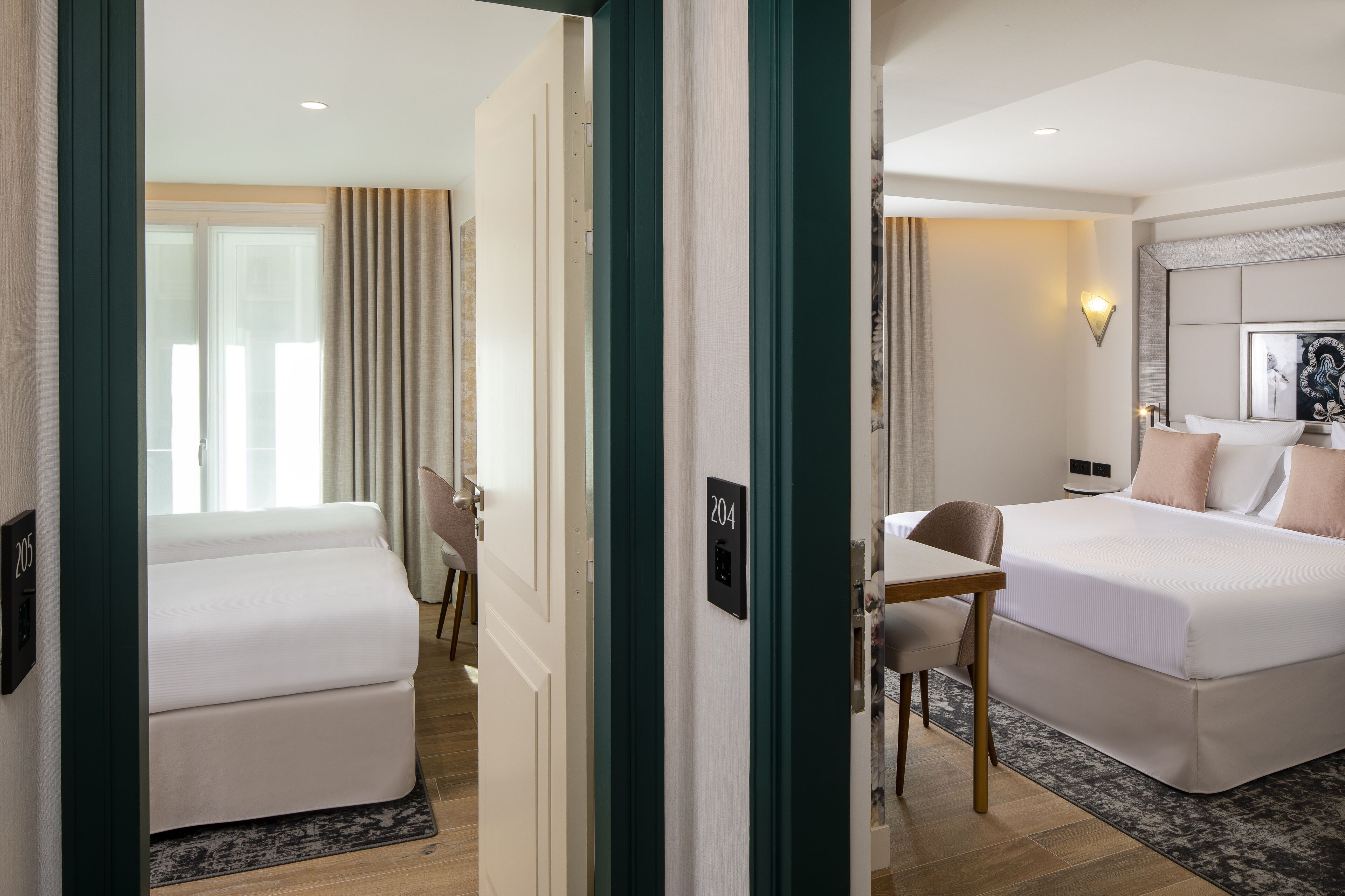 A hotel room with a bed, a desk, and a chair. There is a number on the wall and a light fixture above the bed.