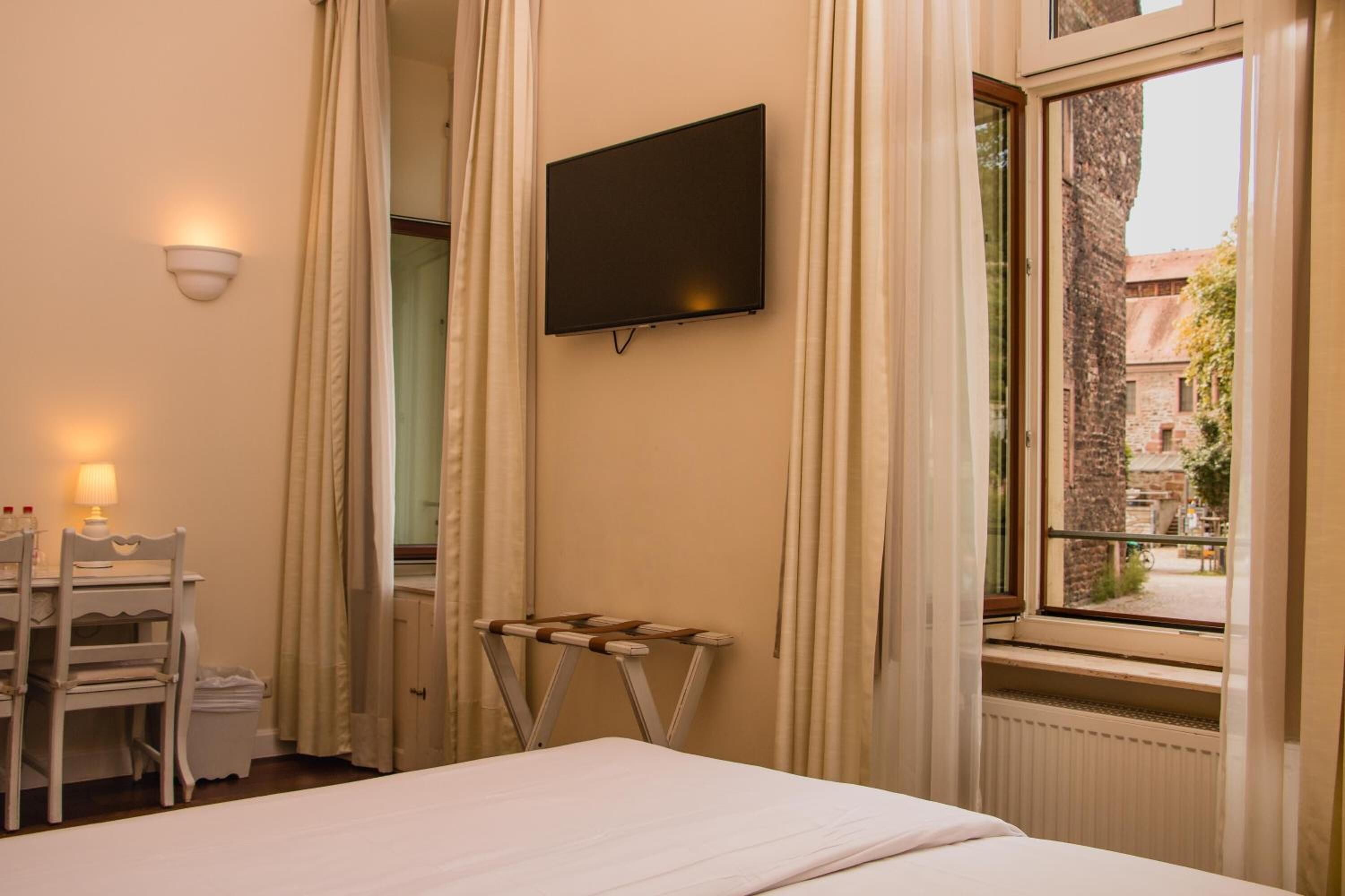 Habitación de hotel con cama, escritorio con silla, televisor montado en la pared y ventana con vistas al exterior.