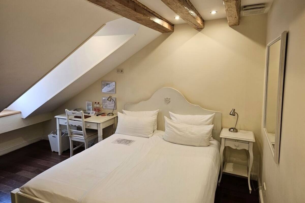A bedroom with a large bed, a desk, and a chair. There is a sloped ceiling and a window.