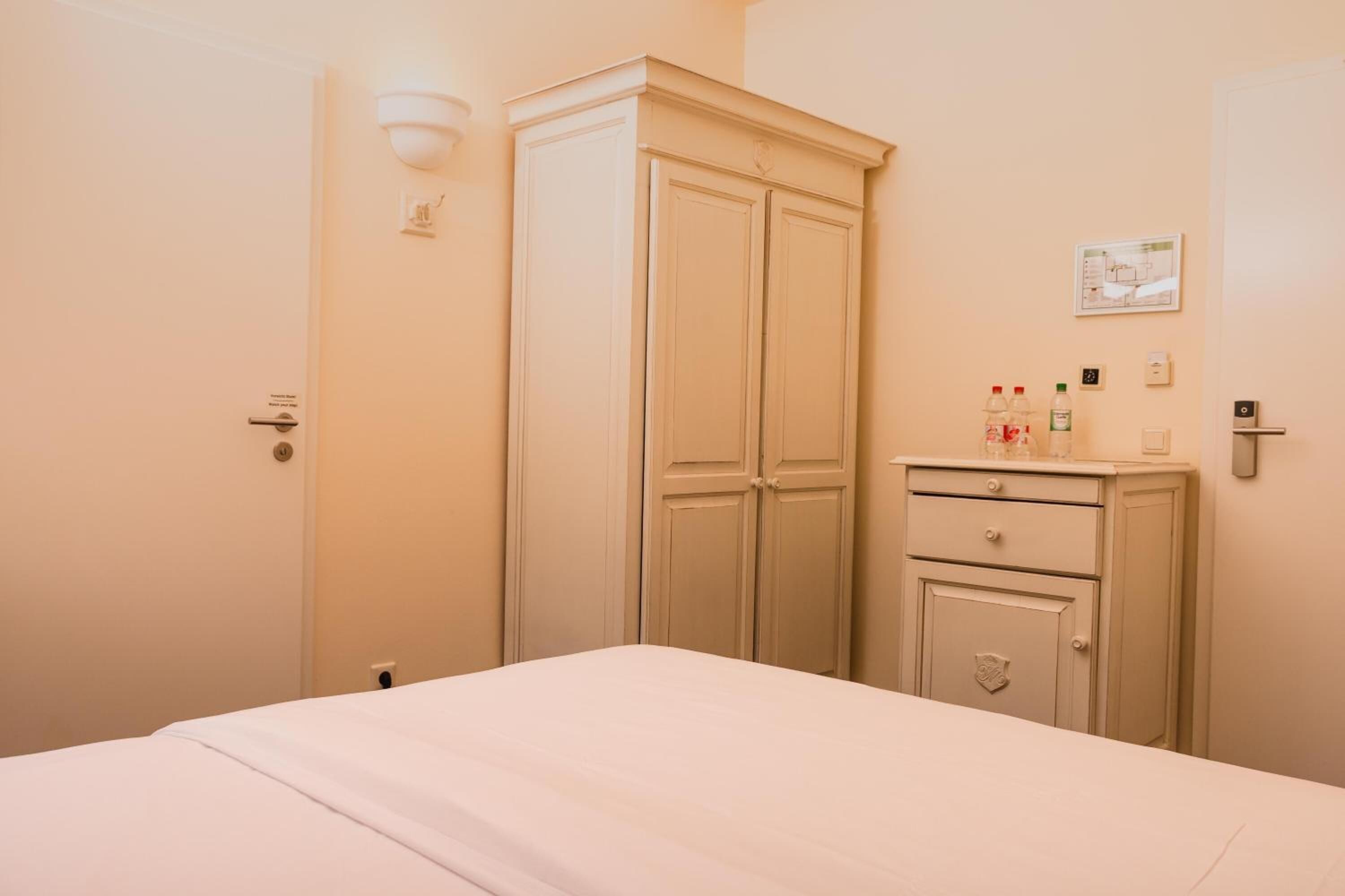 Une chambre à coucher comprenant un lit, une armoire, une table de chevet et un luminaire fixé au mur.