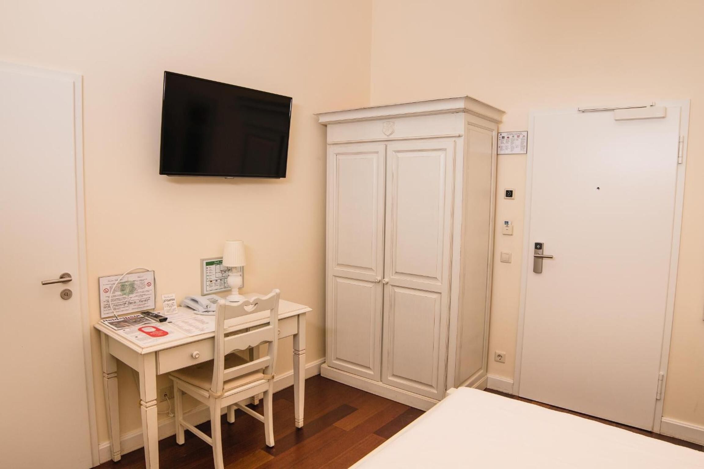 Una habitación con cama, escritorio con silla, televisor y armario.