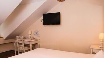 A bedroom with a bed, a desk, a chair, a TV mounted on the wall, and a nightstand with a lamp.