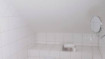 A small, white bathroom with a toilet, sink, and mirror. There are two ceiling lights and a roll of toilet paper on the wall.