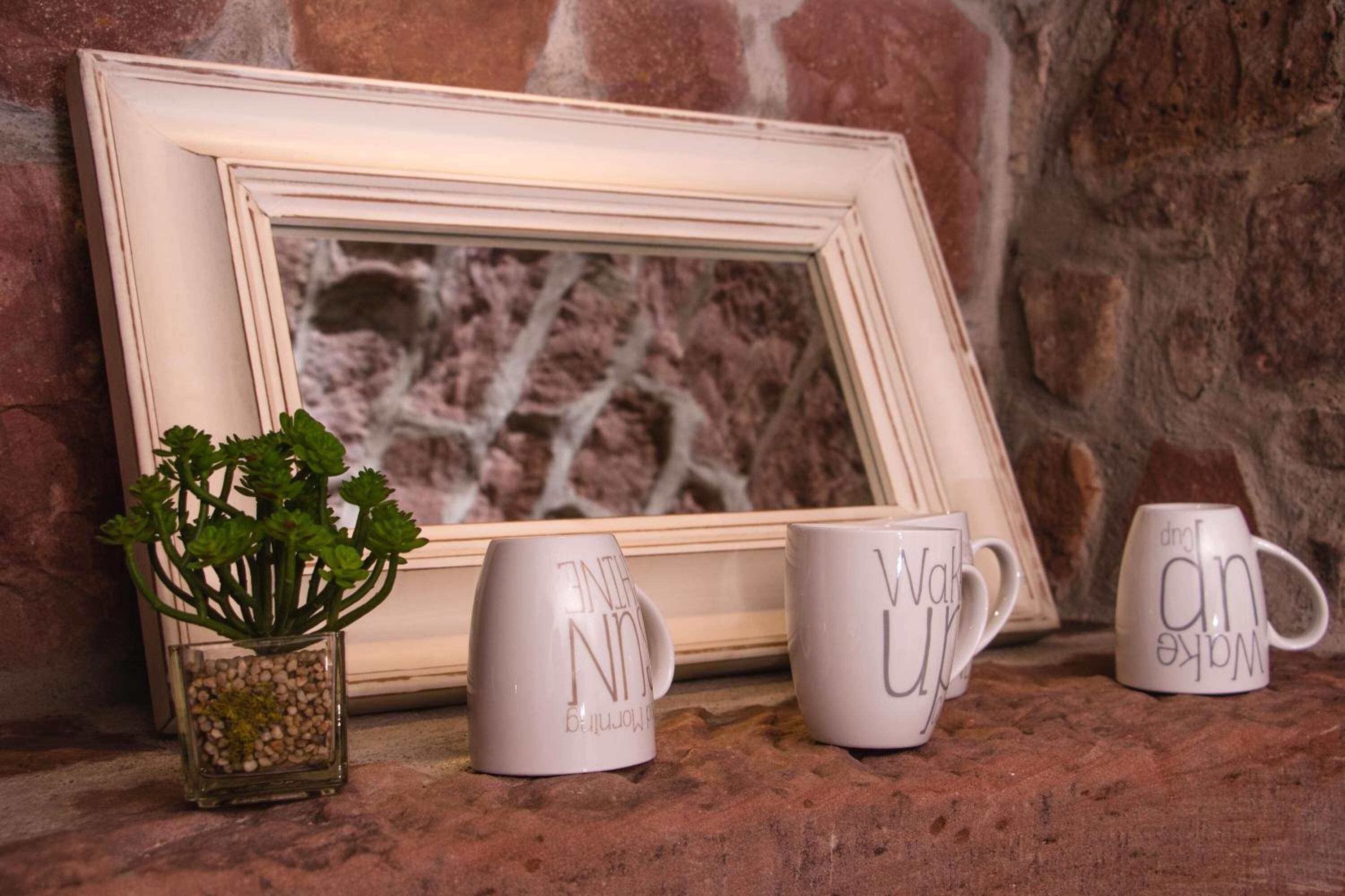 A framed picture with a plant and three mugs on a textured surface.