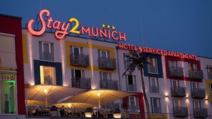 Stay2Munich Hotel & Serviced Apartments met een kleurrijke gevel, een terras en verlichte signage.