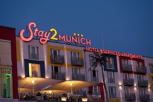 Hotel Stay2Munich y apartamentos con servicios, con fachada colorida, zona de estar al aire libre y señalización iluminada.