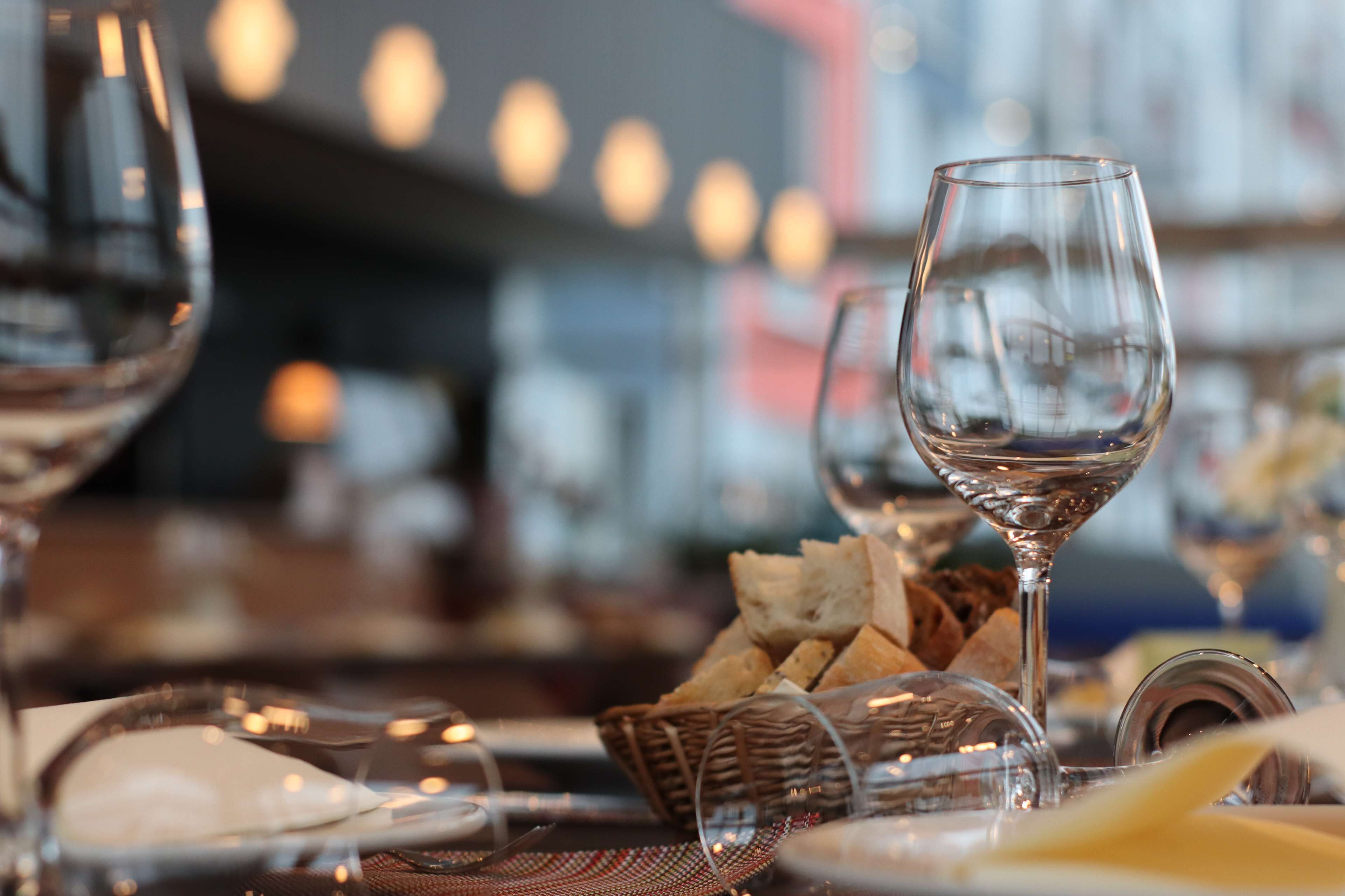 Una mesa de comedor con copas de vino, platos y una cesta de pan.