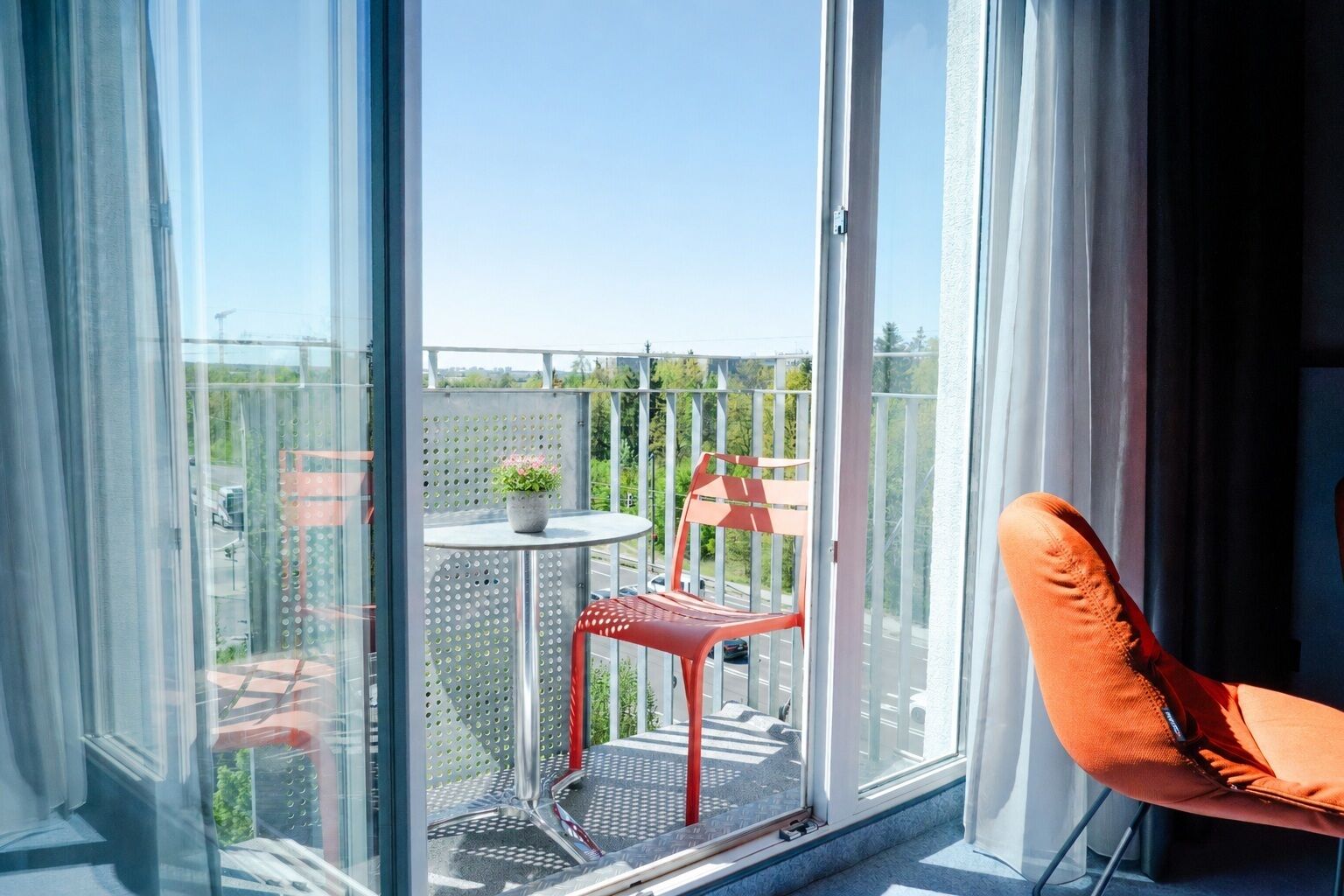 Ein Balkon mit einem roten Stuhl, einem kleinen Tisch und einem Blumentopf.