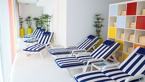 Een zonnige, overdekte ontspanningsruimte met gestreepte lounge fauteuils, een betegelde vloer en een kleurrijk opbergmeubel.