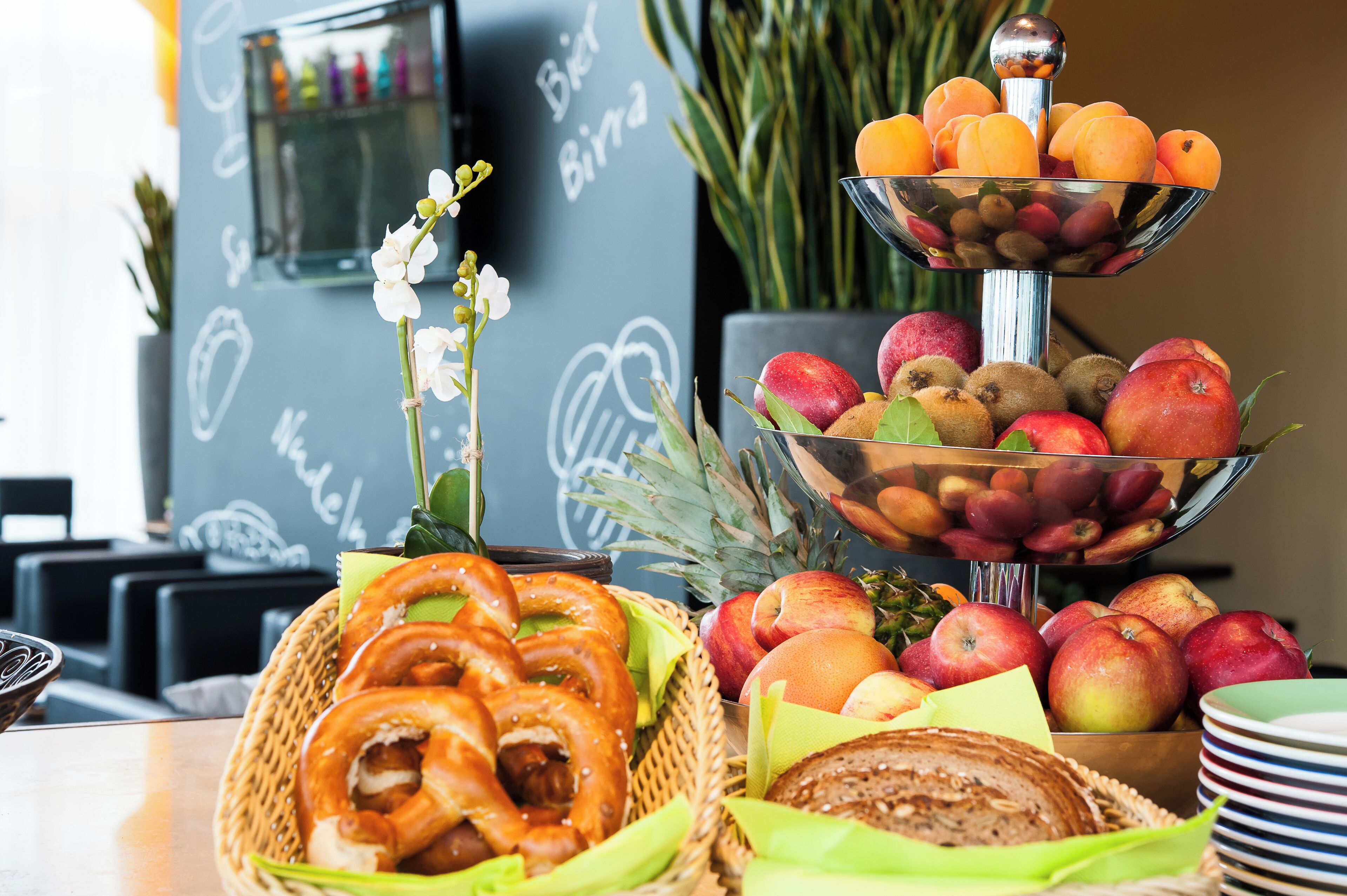 Une table de buffet avec des bretzels, des pommes et un saladier de fruits.