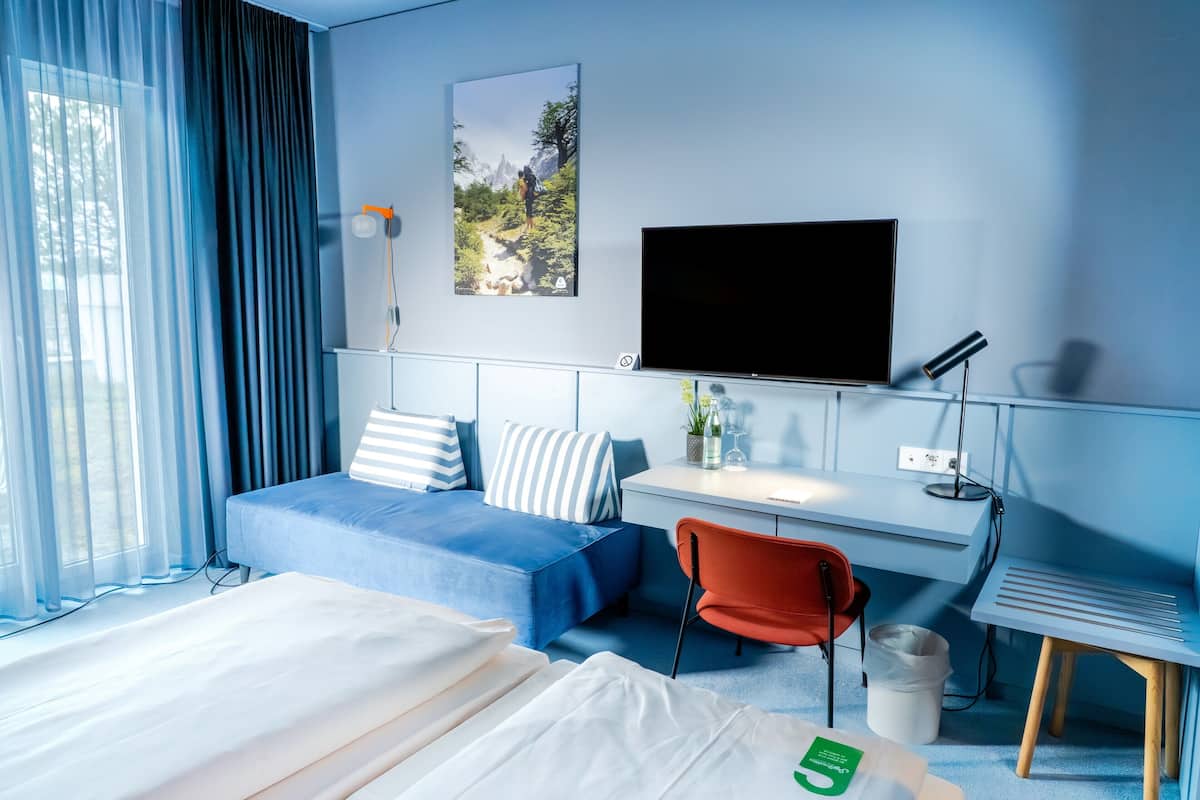 A hotel room with a bed, a desk, a TV, a chair, and a window with curtains.