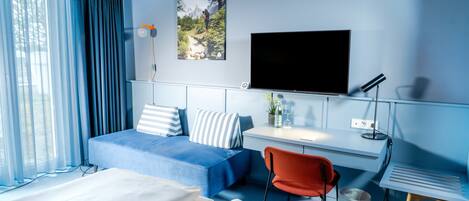 A hotel room with a bed, a desk, a TV, a chair, and a window with curtains.