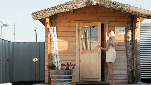 Een houten hutje met rieten dak, een houten deur en een bordje waarop staat dat het een 'Wacholder' en 'Zitronen' hut is.