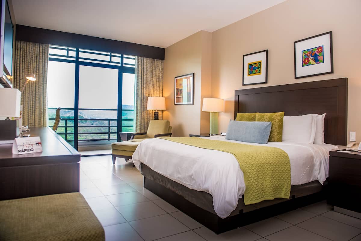 A hotel room with a large bed, a desk, a chair, and a view of the outdoors.