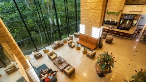 A spacious lobby with a large glass wall offering a view of the forest. There are multiple seating areas and a bar. - Summit Rainforest Golf Resort & All Inclusive (Panama City)