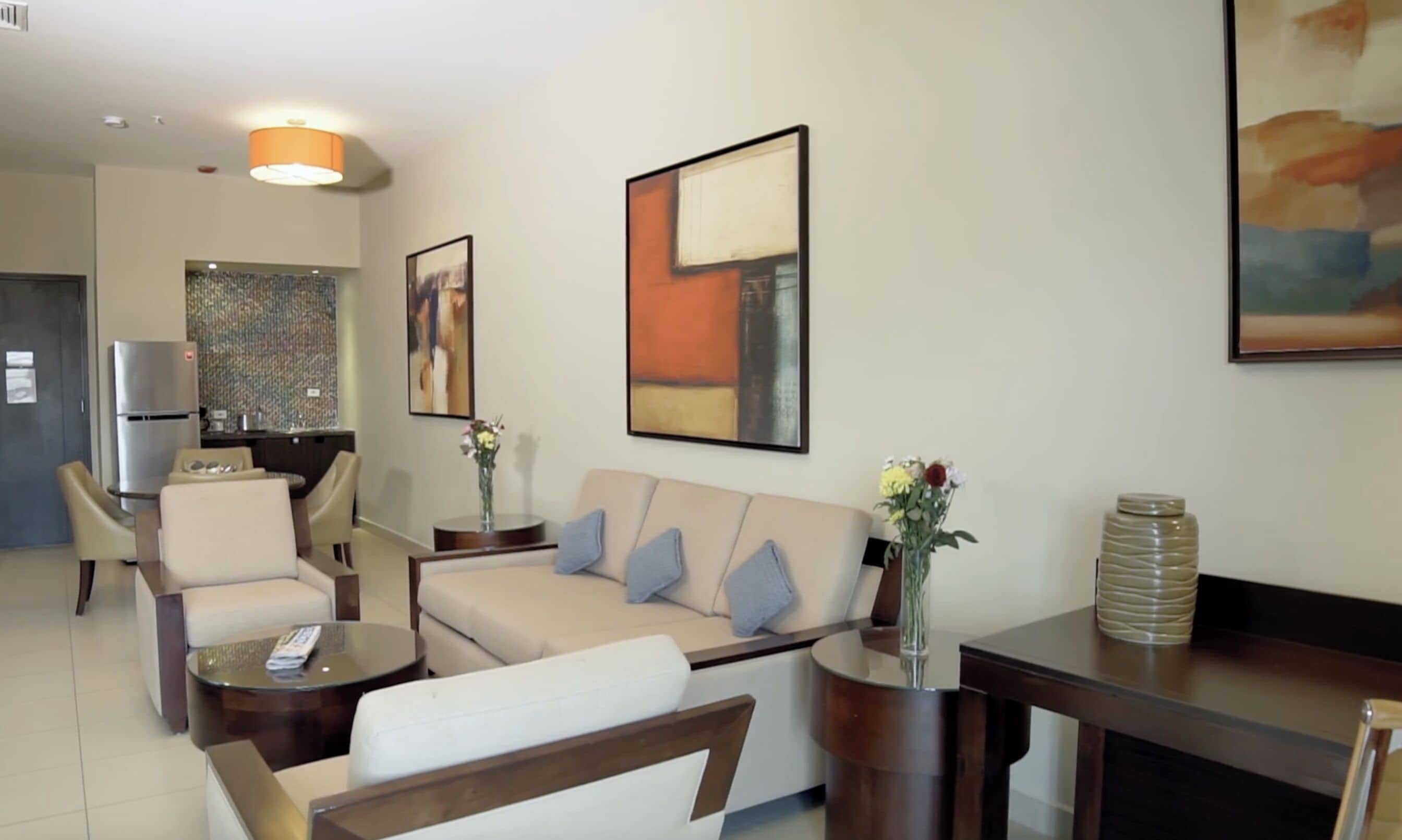 Una sala moderna con un sofá, sillones, una mesa de centro y un comedor con refrigerador.